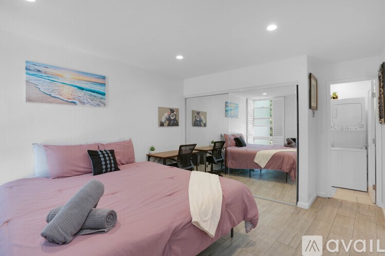 A bedroom with a pink bedspread and a grey towel on the bed.