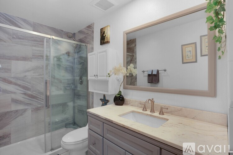 A bathroom with a marble countertop and a glass shower enclosure.