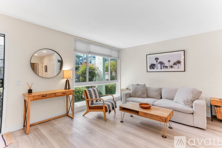 A living room with a grey couch, a wooden desk, a chair, and a framed picture on the wall.