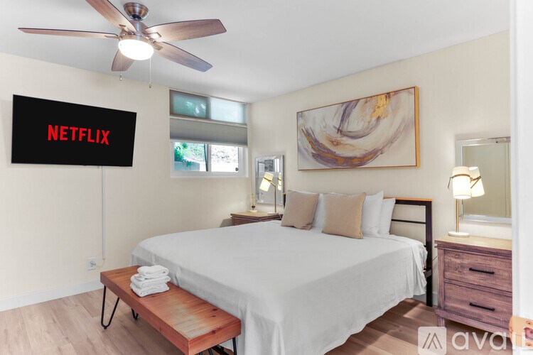 A bedroom with a bed, a bench, a ceiling fan, and a painting on the wall.