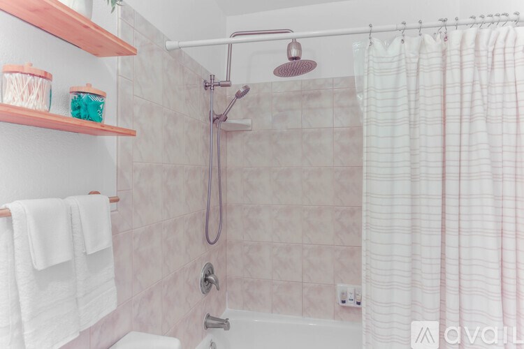A bathroom with a shower curtain, a towel rack with towels, and a shelf with containers.
