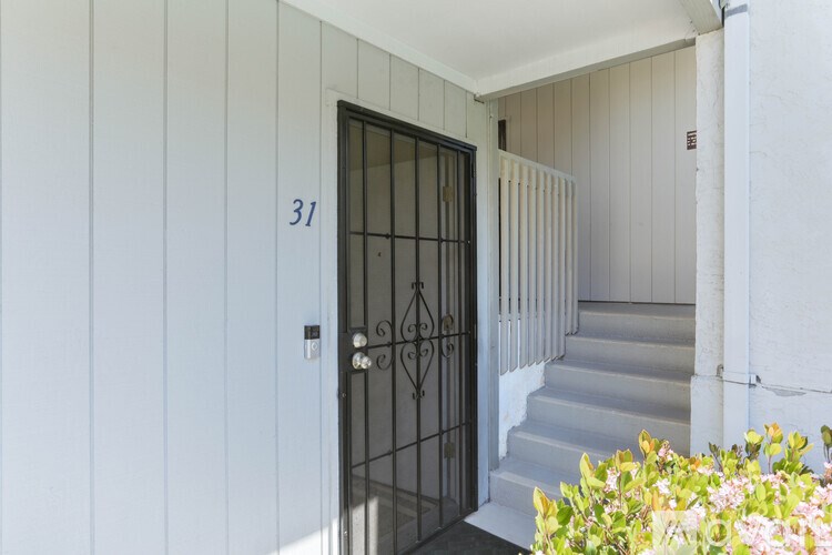 A black door with a metal grill is on the left side of a white wall with a number 31 on it.