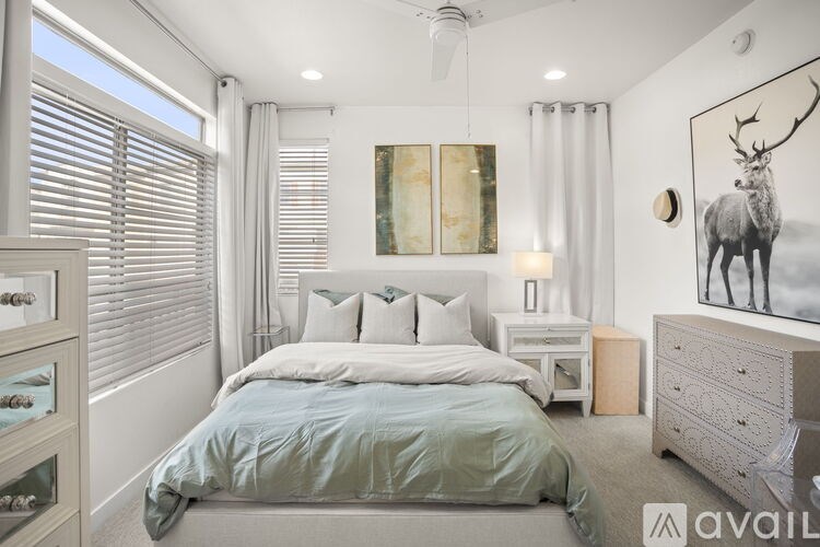 A bedroom with a large bed, a dresser, and a painting of a deer on the wall.