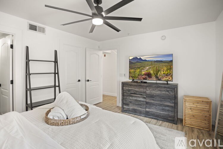 A bedroom with a white bed, a wooden dresser, and a painting of a landscape on the wall.