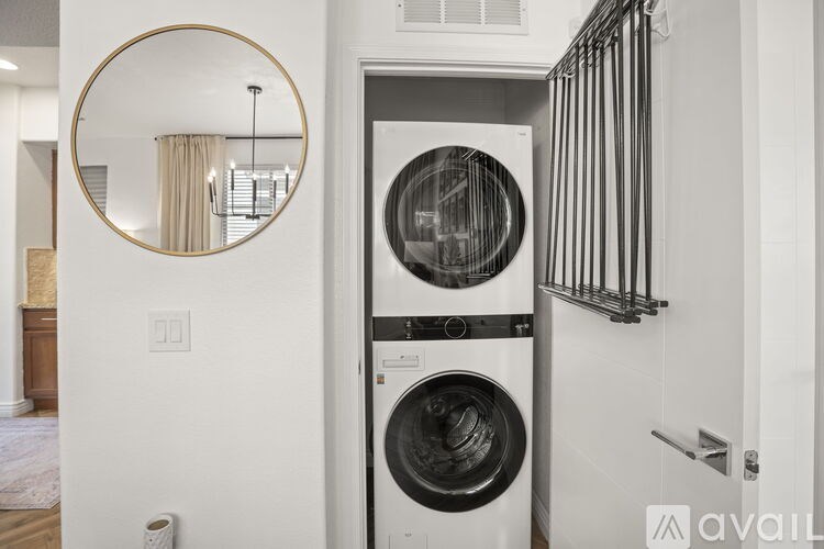 A white wall with a round mirror and a washing machine in front of it.
