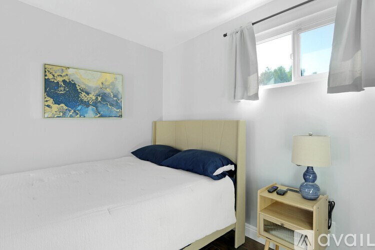 A bedroom with a bed, nightstand, and a painting on the wall.