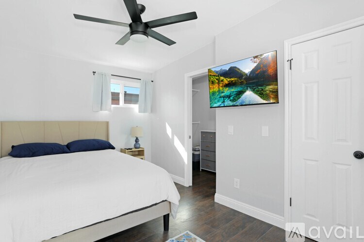 A bedroom with a bed, a ceiling fan, and a painting on the wall.