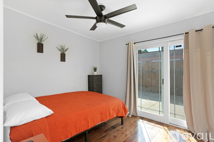 A bedroom with a bed, a ceiling fan, and a sliding glass door.