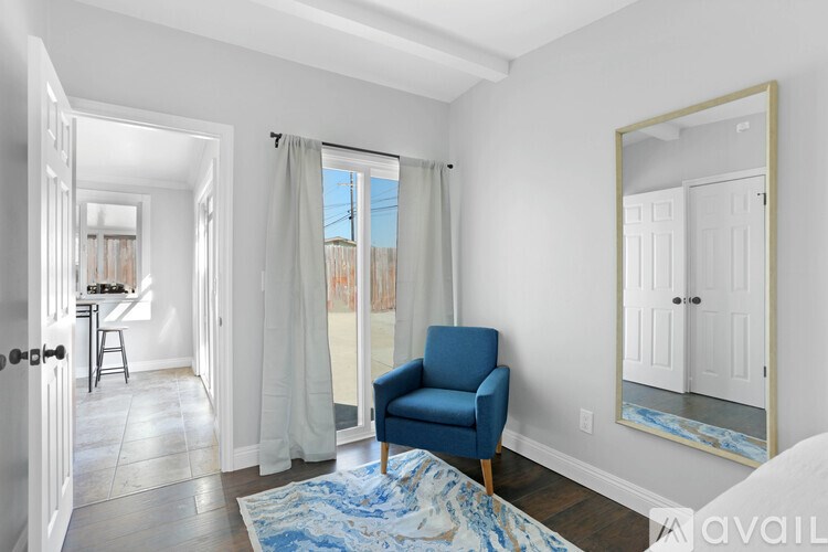 A blue chair sits in a white room with a mirror and a rug.