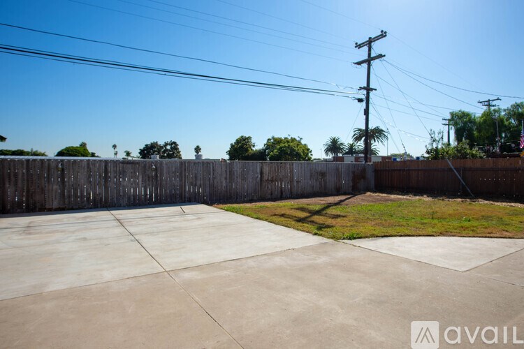 A concrete driveway leads to a wooden fence with a clear blue sky above.