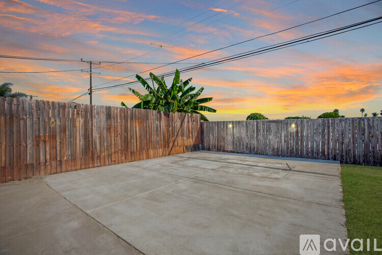 A concrete driveway leads to a wooden fence with a palm tree in the background.