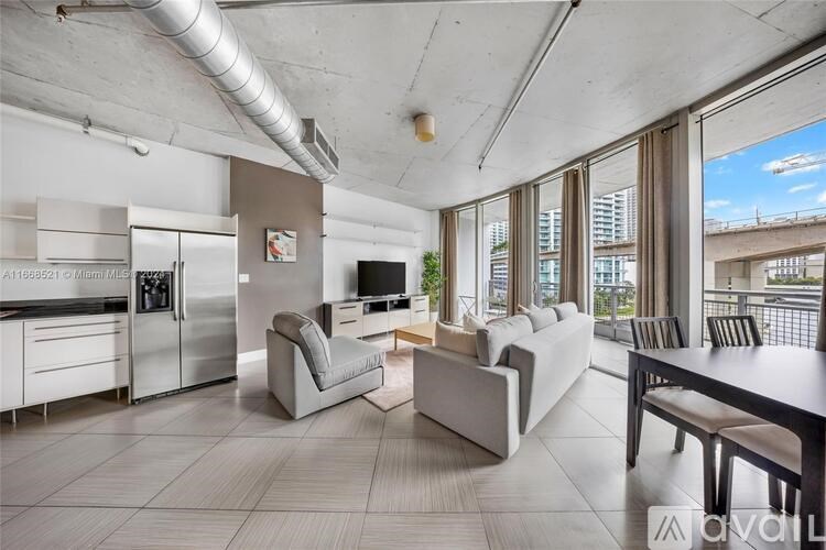 A modern kitchen with a refrigerator, a dining table with chairs, and a living area with a couch.