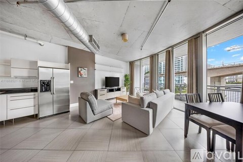 A modern kitchen with a refrigerator, a dining table with chairs, and a living area with a couch.