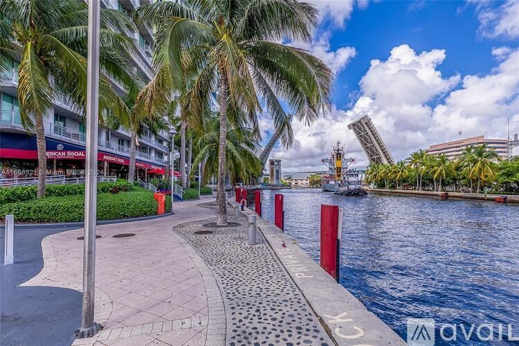 A walkway next to a body of water with palm trees and a building in the background.