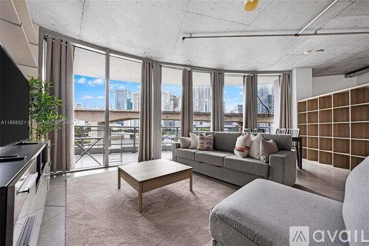 A living room with a grey sofa, a wooden coffee table, and a large window with a view of the city.