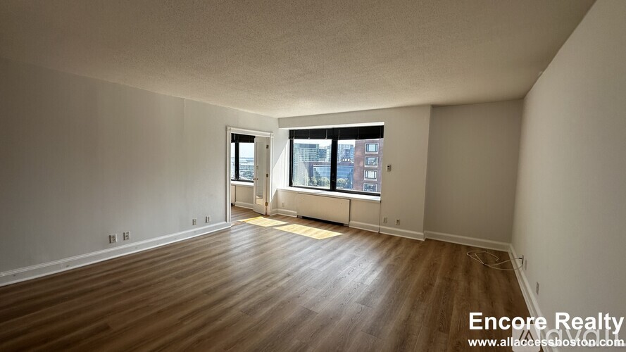 A room with wooden flooring and a window overlooking a city street.