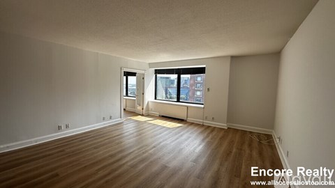 A room with wooden flooring and a window overlooking a city street.