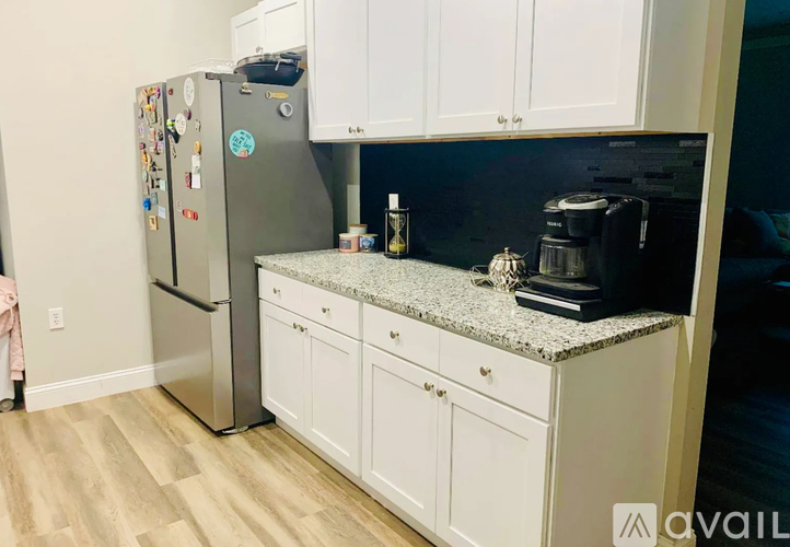 A kitchen with a refrigerator covered in magnets, a granite countertop, and white cabinets.