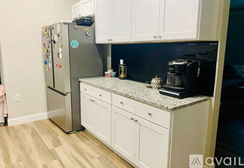 A kitchen with a refrigerator covered in magnets, a granite countertop, and white cabinets.