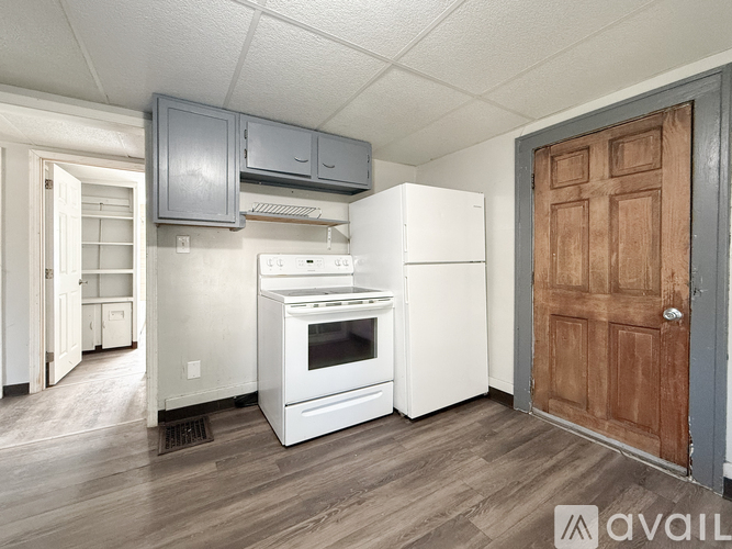 A kitchen with a white fridge and oven, a wooden door, and a white ceiling.