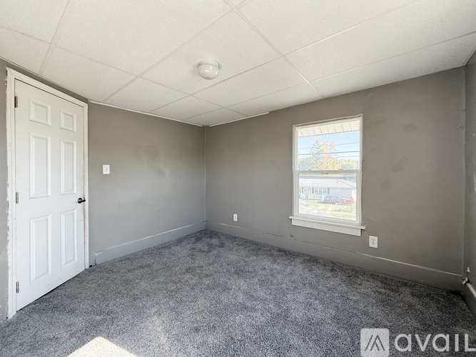 A room with a carpeted floor, a door, a window, and a ceiling light.