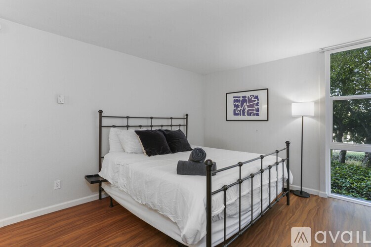 A bedroom with a white bed and a window overlooking a green area.