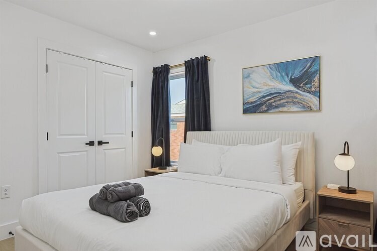 A bedroom with a large bed, two windows with curtains, and a painting on the wall.