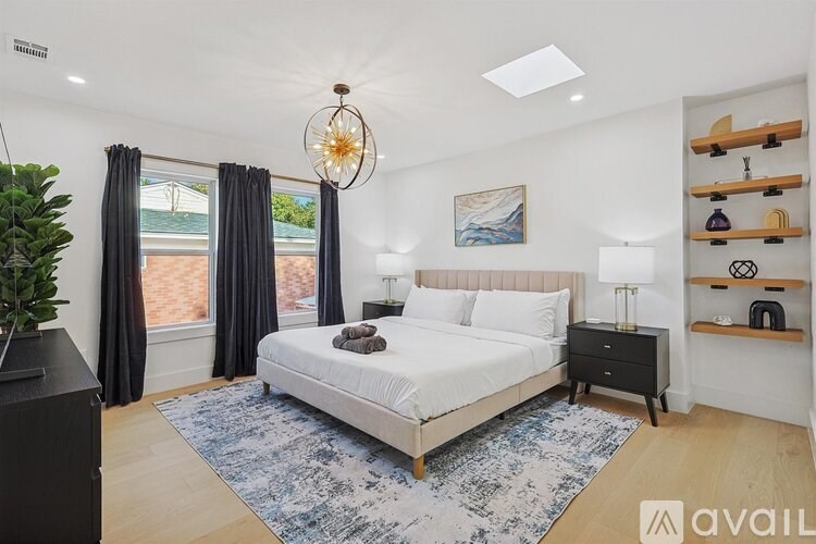 A bedroom with a large bed, a plant, and a painting on the wall.