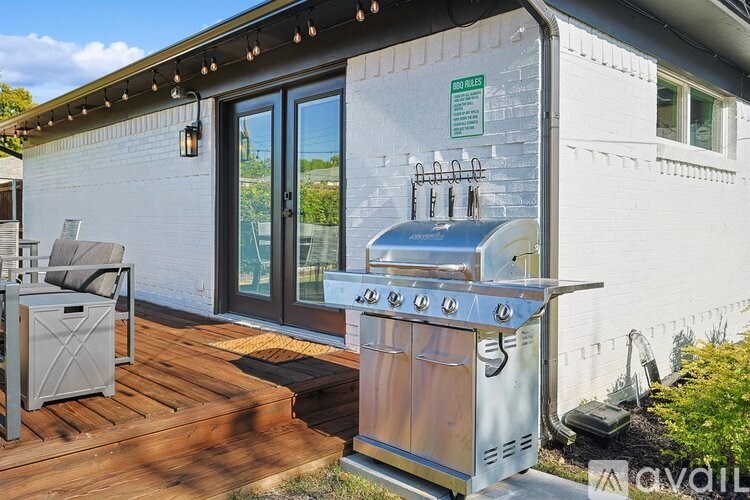 A BBQ grill is on a wooden deck outside a house.