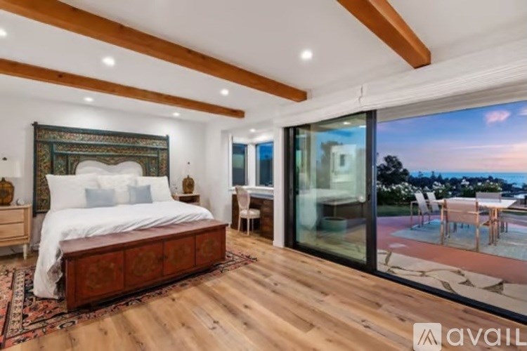 A bedroom with a large bed and a view of the outdoors through a glass door.