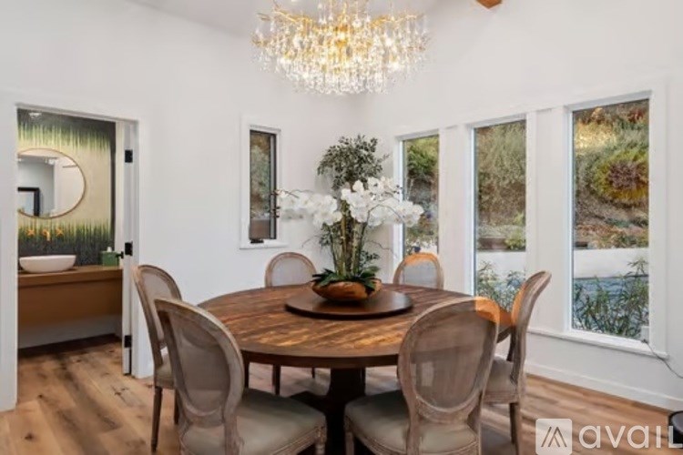 A dining room with a wooden table and chairs, a chandelier, and a view of the outdoors through the windows.