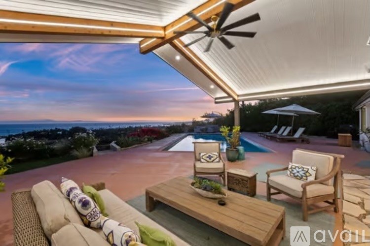 A patio with a table, chairs, and a ceiling fan overlooking a pool.
