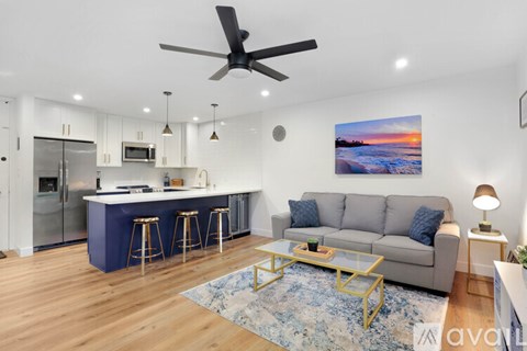 A modern kitchen with a bar area and a living room with a couch and a painting on the wall.