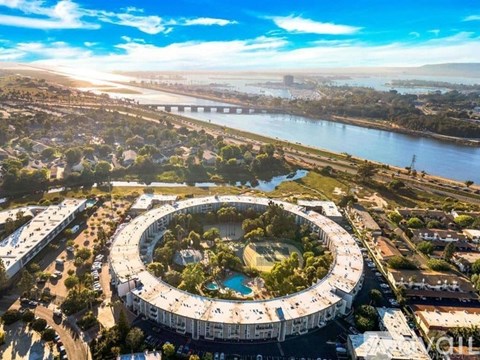 A large circular building with a pool in the middle is surrounded by a road and greenery.