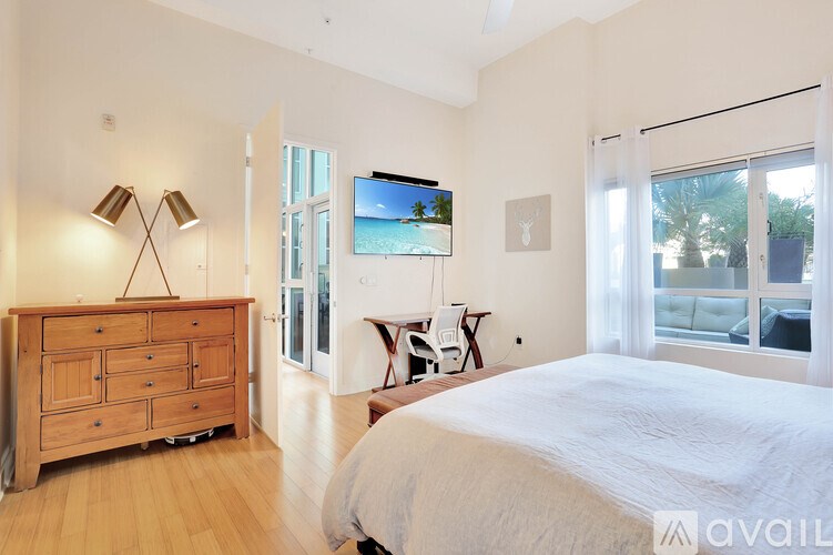 A bedroom with a large bed, a wooden dresser, and a flat-screen TV mounted on the wall.