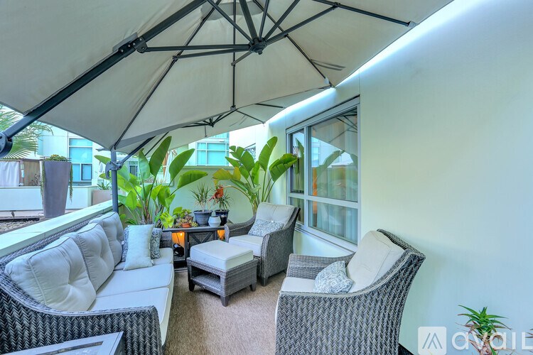A patio with a white couch, grey wicker chairs and a table with a candle on it.