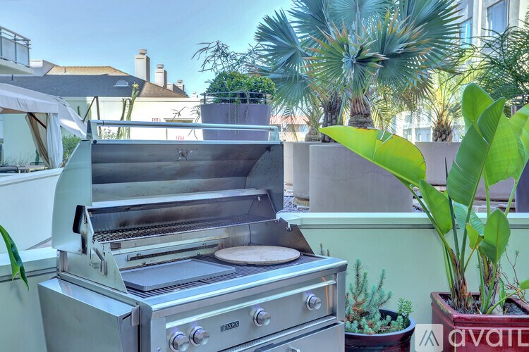 A stainless steel grill is on a balcony with plants around it.