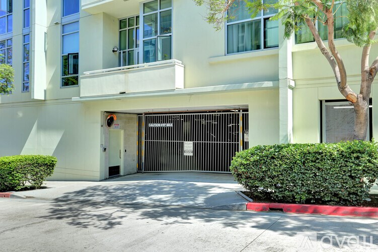 A white building with a black gate and a tree in front.