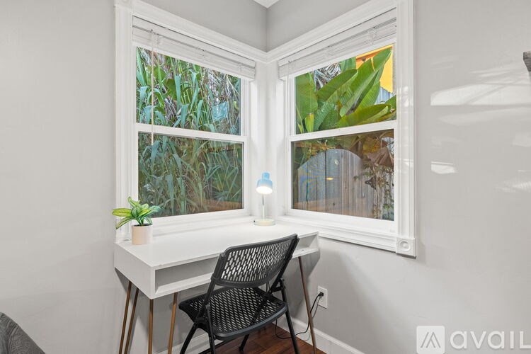 A white desk with a chair and a potted plant sits in front of a window with a view of greenery.
