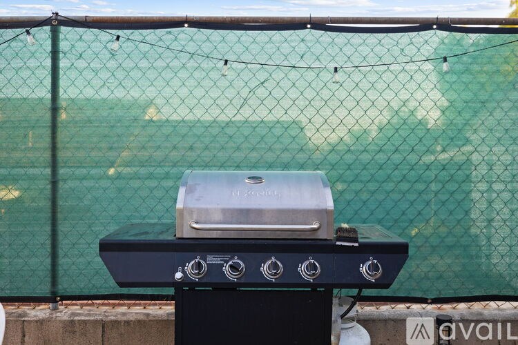 A Weber grill is on a stand with a green fence in the background.