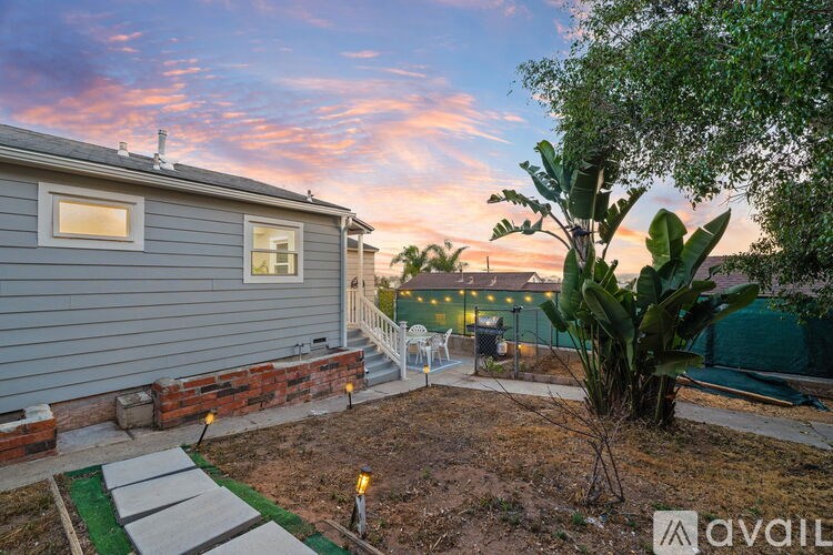 A backyard with a grey house, a tree, and a small patio area.