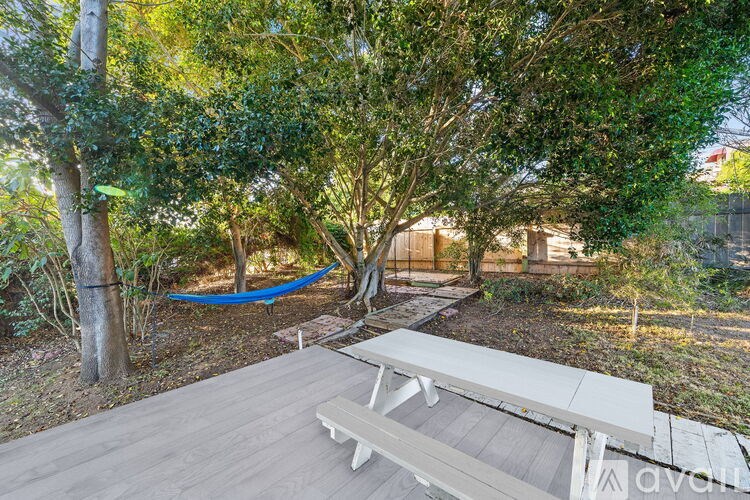 A wooden picnic table is in the middle of a backyard with a blue hammock between two trees.