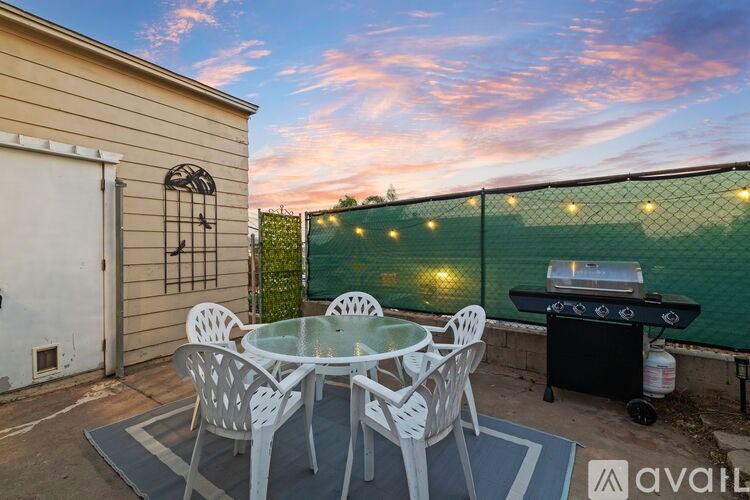 A patio with a table and chairs is set up on a patio with a grill and string lights.