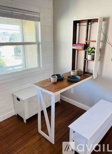 A small white desk with a wooden top and white chair in a room with a window.