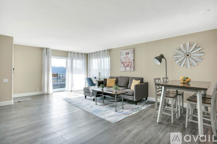 A living room with a grey couch, a coffee table, and a large window with curtains.