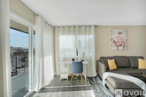 A living room with a grey couch, a small table with a blue chair, and a painting on the wall.