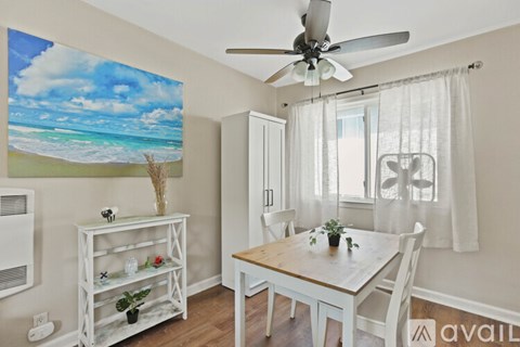 A dining room with a white table and chairs, a ceiling fan, and a beach scene on the wall.
