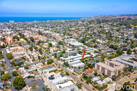 A bird's eye view of a city with buildings, roads, and a red arrow pointing to a specific building.
