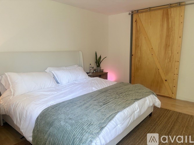 A bed with white pillows and a grey blanket in a room with a wooden door.
