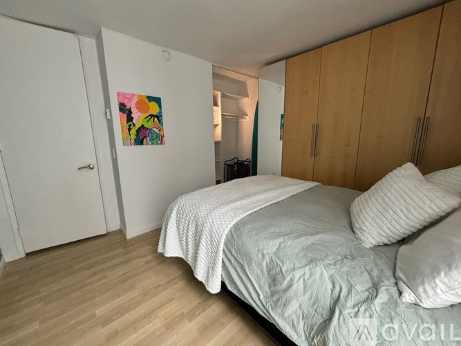 A bedroom with a bed, pillows, and a painting on the wall.